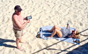 Pareja de lectores con dispositivos Kindle en la playa. 